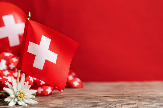 Swiss flag with edelweiss flower and red ribbons on wooden table. National Day background with copy space.
