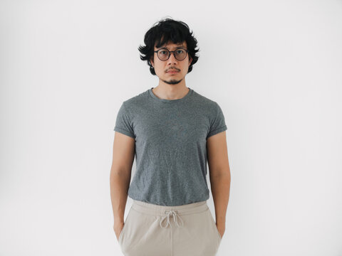 asian man relaxed asian man wearing grey tshirt standing against white backdrop, confident asian male model in casual attire with neutral expression isolated on white background