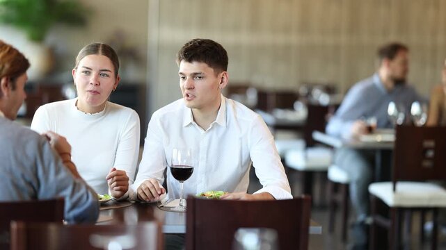 Three friends meeting in modern restaurant - men and a woman drinking wine, talking, discussing problems. High quality 4k footage