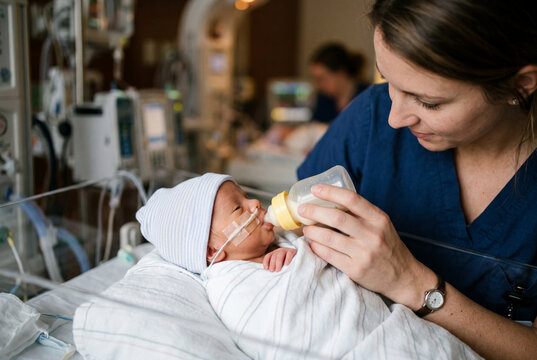 Nurse gently bottle feeding a premature baby with a feeding tube in a hospital
