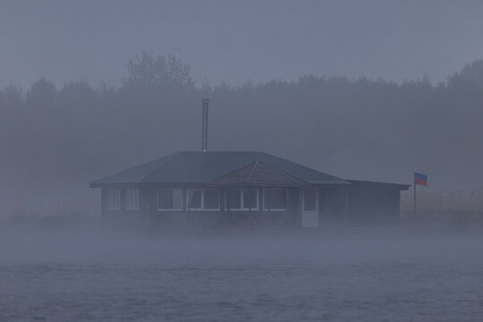 Wooden birdwatching and fishing cabin on wooden stilts shrouded in thick morning fog on Lake Chaika at Curonian Spit