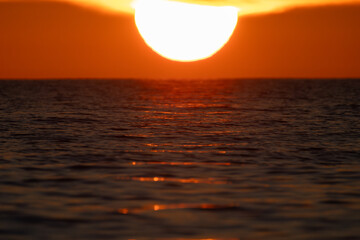 Extreme close-up of a massive bright sun dipping below the sea horizon during a spectacular golden sunset