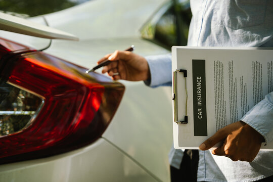 Close-up of an insurance agent inspecting a car and holding a car insurance document during a vehicle assessment, representing auto insurance claims, inspection, and customer service.