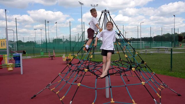 Two children, a boy and a girl, climbing a rope web playground structure during active outdoor play. The footage shows physical activity, coordination, balance, and adventurous childhood play on a mod