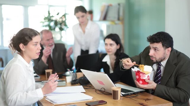  Male manager eats noodles in office and spreads unpleasant smell of food, outraged colleagues express dissatisfaction. Repulsive smell of food filled office