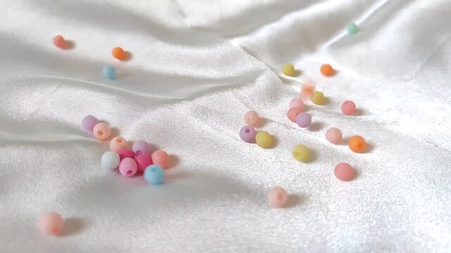 Colorful Pastel Beads Falling in Super Slow Motion on White Silk