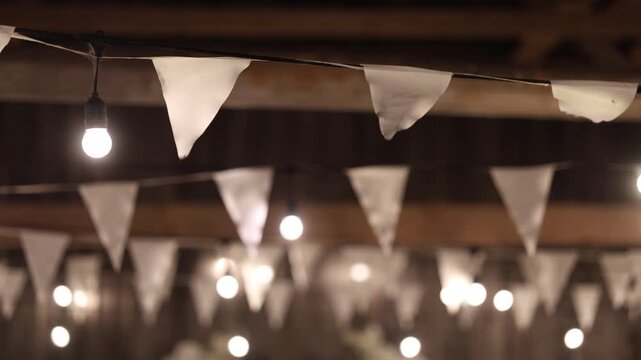 White fabric pennants hang beside glowing bulbs under wooden beams, creating a warm festive indoor scene