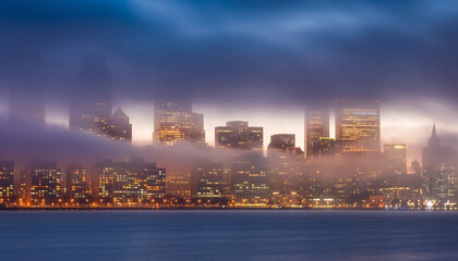 Naklejka premium A dense layer of fog partially obscures a brightly lit metropolitan skyline across dark water during twilight hours.