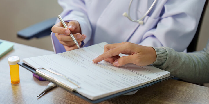 Cropped hands of doctor and patient reviewing medical form on clipboard for healthcare consultation