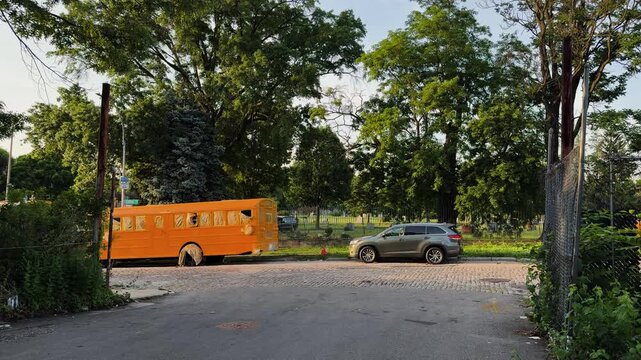 Weathered yellow school bus parked in open lot surrounded by trees, Bushwick