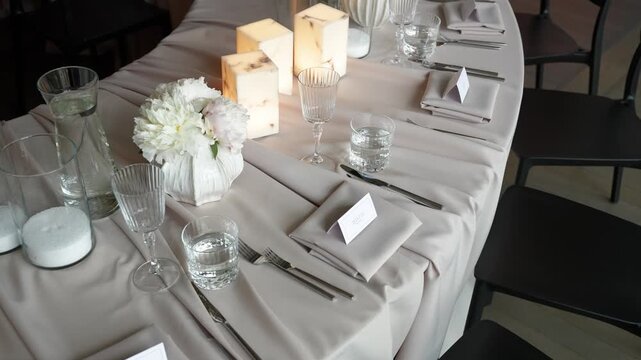 Beautifully arranged dinner table with white flowers, glowing pillar candles, crystal glassware, and minimalist place cards in soft natural light&mdash;perfect stock footage for events, weddings.