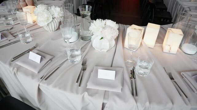 Elegant table setting with white floral centerpieces, glowing candles, glassware, and name cards in a refined, softly lit reception room, perfect for weddings or formal dinner events.