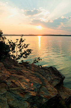 Summer sunset landscape, picturesque summer time nature view, scenic dramatic sunset sky over the water surface and stone bank of the lake on the foreground