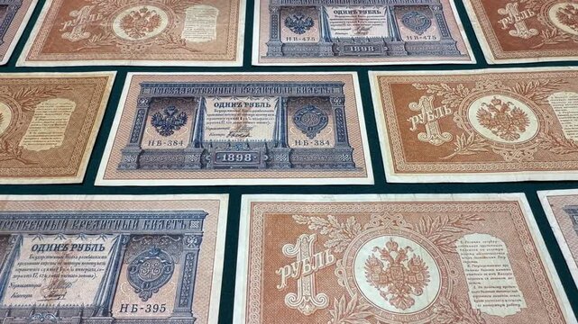 Assorted antique 1 ruble 1898 Russian Empire banknotes arranged in a neat pattern, showing ornate details, faded paper texture and historic money design on a flat surface.