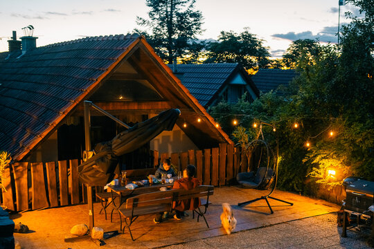 Evening gathering at a backyard table near a cabin with string lights and a dog running around