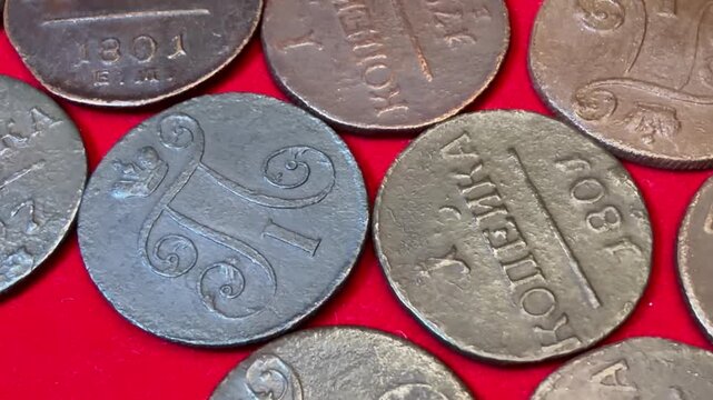 Close-up of old copper 1 kopeck coins 1797-1801 Russian Empire Paul I scattered on bright red fabric, showing worn details, numbers and lettering, ideal for history, money.