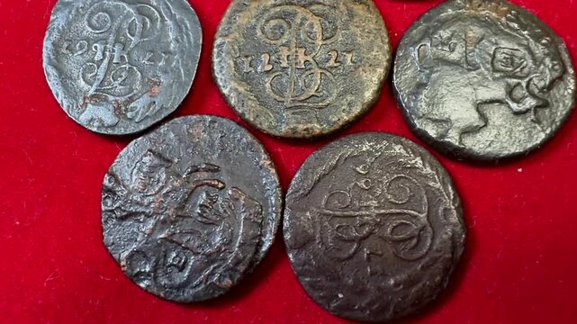Close view of old worn Polushka coins 1766-1796 Russian Empire Catherine II on red fabric, showing aged metal texture, engraved symbols and a vintage collectible look.