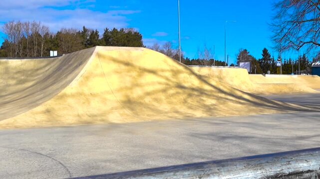 Empty concrete skatepark with ramps and grinding rail waiting for skaters and BMX riders under a clear blue sky, a perfect location for practicing extreme sports and urban recreation