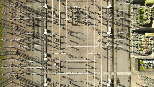 Drone view of a high voltage electrical power substation with transformers and insulators for energy transmission, highlighting the complex network of cables and industrial equipment