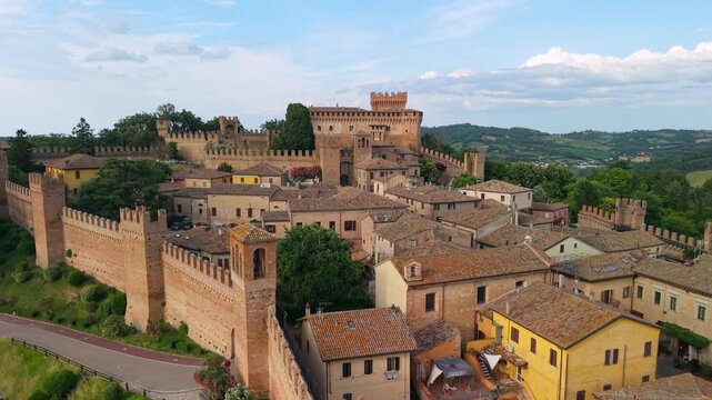 Gradara Castle Marche Italy 4K Drone. Backward flight reveal from medieval towers of compact fortified borgo town among green hills. Borghi piu belli d Italia most beautiful villages video asset