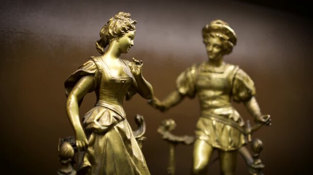 A close-up of a golden bronze statue of a boy and girl figurine displayed as a decorative ornament on a dark background.