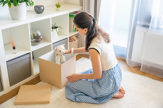 Young woman taking old stuffed toy from storage box in home interior. Home organization and decluttering with childhood memories concept