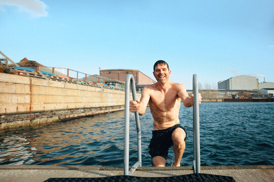A ladder helps the man continue swimming as he climbs from the cold water by the dock.