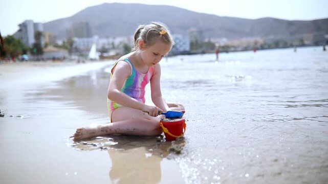 Little girl in a colorful swimsuit playing with sand toys on Los Cristianos beach in Tenerife, Canary Islands, Spain