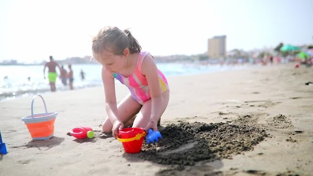 Little girl in a colorful swimsuit playing with sand toys on Los Cristianos beach in Tenerife, Canary Islands, Spain