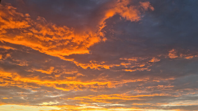 Orange and grey clouds illuminated by sunset light across evening sky. Cloudscape photography. Wide sky view with copy space