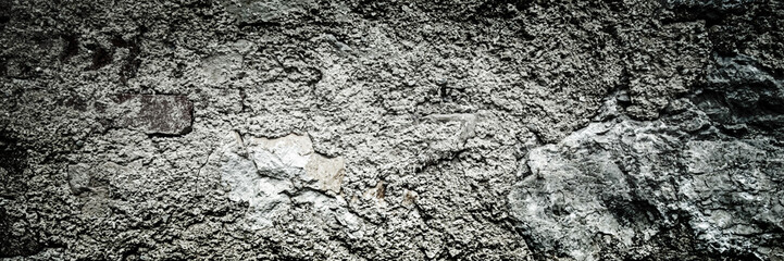 Fototapeta premium A wide black and white panoramic full-frame texture background of an ancient weathered stone wall