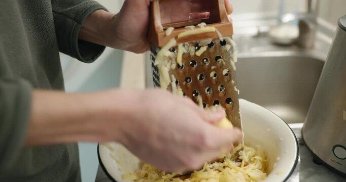 Caucasian man grate potato. Single male is cooking at kitchen at home. 4K 10-bit