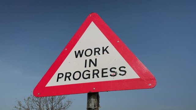 Camera orbiting around a triangular work in progress warning sign against a clear blue sky The road safety marker highlights ongoing construction activity and infrastructure development
