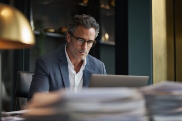 Obraz premium Businessman with glasses working on laptop in modern office. Focused manager typing on computer. Professional career and corporate workplace concept. Serious executive analyzing data.