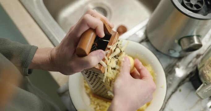 Caucasian man grate potato. Single male is cooking at kitchen at home. 4K 10-bit