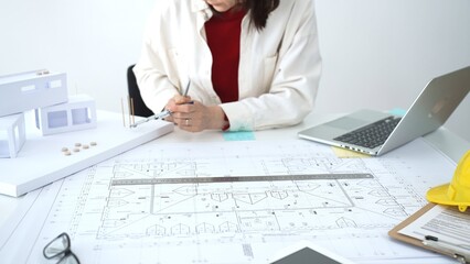 Naklejka premium Architect working on construction blueprints and architectural models, planning a new residential building project with an eye on modern design and urban development