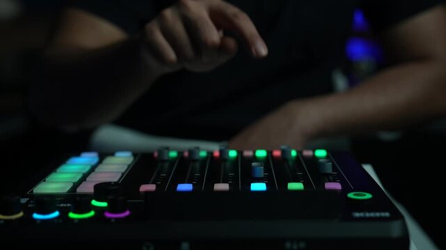 Hand operating illuminated audio mixer sliders in a dimly lit studio environment
