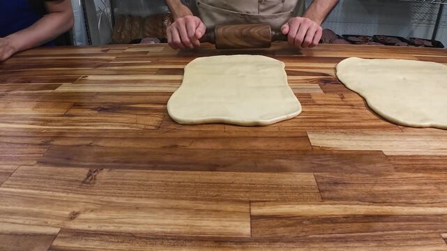skilled baker focuses on precision, rolling out and flattening dough into a perfect rectangle on a wooden table to prepare artisanal bread loaves.