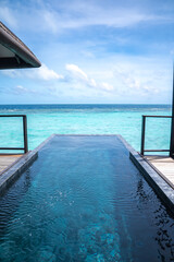 Obraz premium An infinity plunge pool reaches a turquoise lagoon by an overwater villa in the Maldives. Clean lines, central vanishing point, and bright sky suggest calm and luxury.