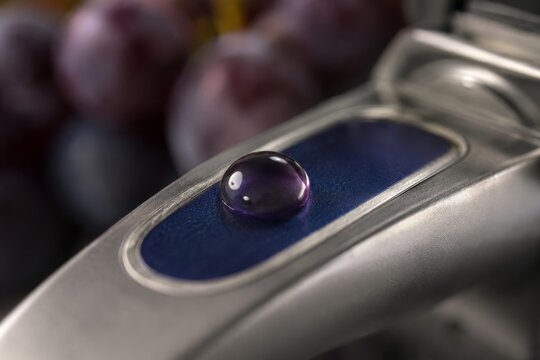 Refractometer testing grape juice drop on metal prism. Winemaker measuring sugar level of grape harvest for wine production. Quality control process in modern winery cellar laboratory.