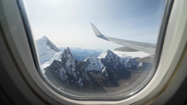 Cruising aircraft shifting wing and peaks across cabin window frame, showing glaciers and glare