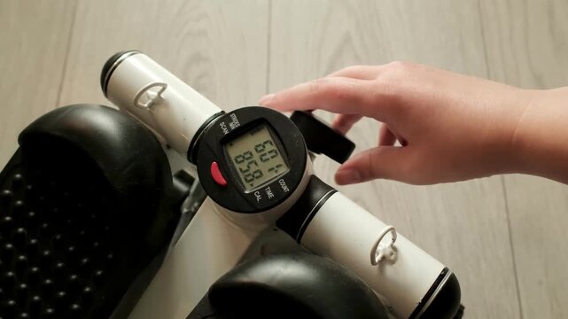 Hand adjusting the resistance control knob on a mini stepper exercise machine. Concept of workout customization, fitness equipment settings, and personalized training.