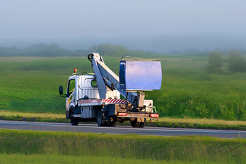 Infrastructure maintenance truck with boom lift near open field © AlexGo