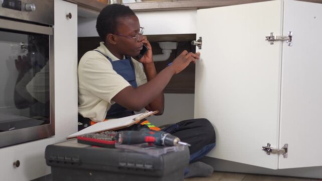Black female plumber talking on the phone in a kitchen