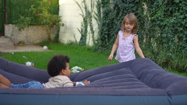 Little girl jumping on an inflatable mattress next to a boy lying down