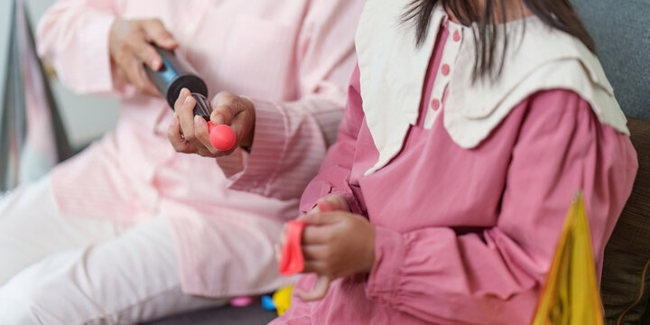 Grandmother and granddaughter inflating balloons with hand pump for birthday party preparation