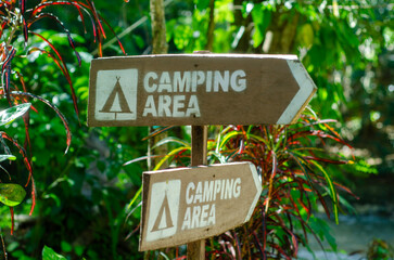 Fototapeta premium Brown wooden signs indicate camping area direction against a backdrop of vibrant green forest foliage for outdoor recreation planning