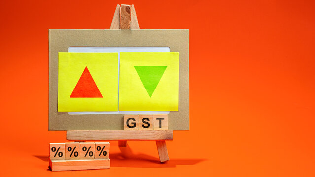 An easel displaying GST blocks with up and down arrows on sticky notes and percentage symbols against an orange background, representing tax rate changes