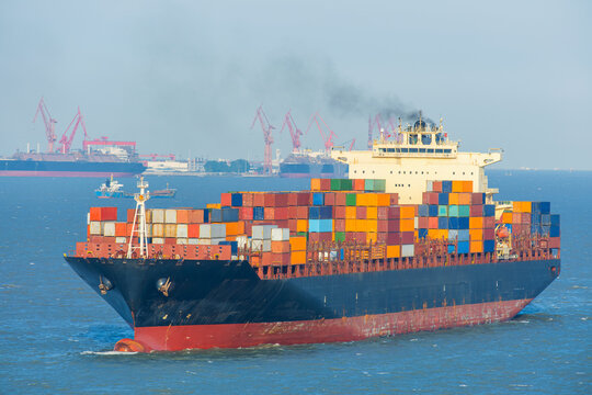 Container ship loaded with multicolored freight containers sailing near Shanghai port facilities. International maritime trade, global logistics, cargo transportation, import export operations