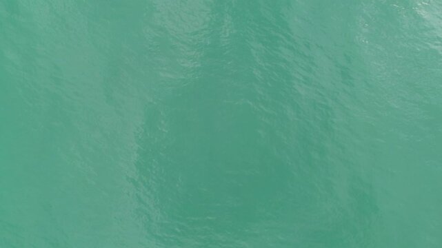 A top-down aerial drone shot of smooth, clear turquoise sea water gently rippling near the Batumi coastline on the Black Sea in Georgia. The overhead perspective creates an abstract, visually striking